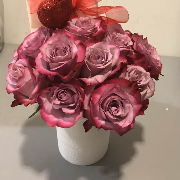 Pink roses in a white vase with a red ribbon and heart decoration