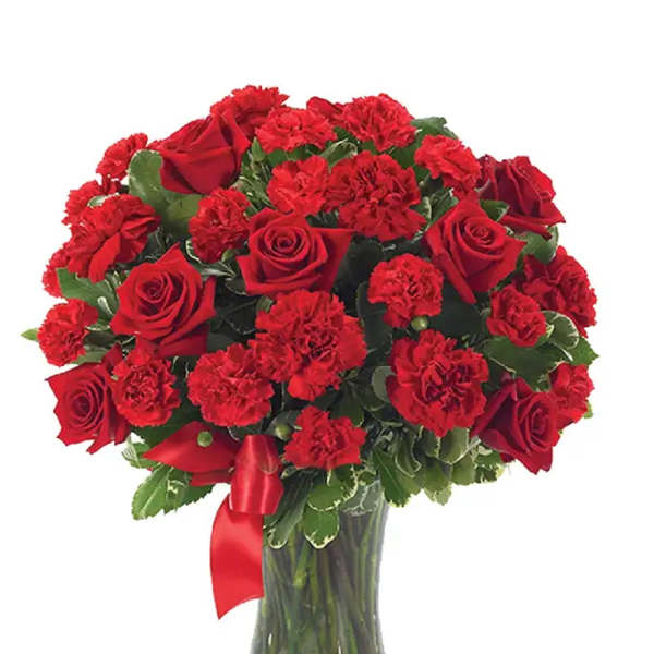 Red roses and carnations arranged in a clear glass vase with a red ribbon