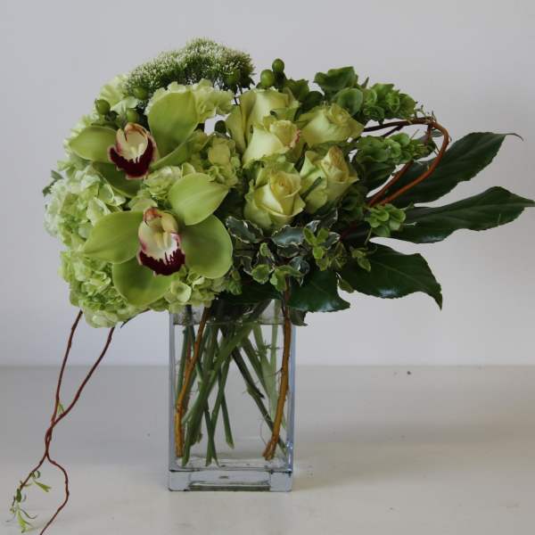 Green orchid and rose arrangement with hydrangeas in a clear rectangular glass vase