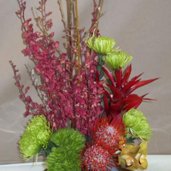 Tall floral arrangement in a brown square container with bright green, red, and pink blooms