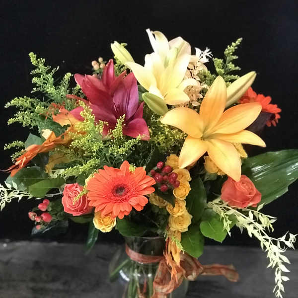 Mixed bouquet of lilies, gerbera daisies, and roses in a glass vase
