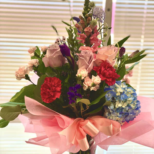 Mixed bouquet of pink roses, carnations, and blue hydrangea in a glass vase