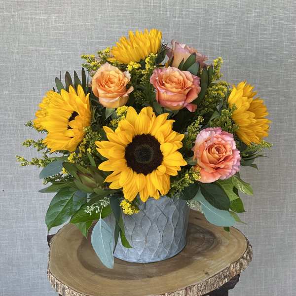 Sunflowers and peach roses in a metal container