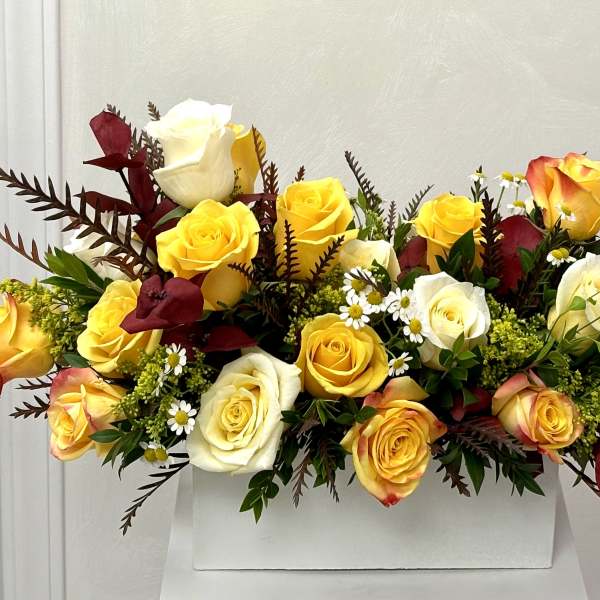 Yellow and white roses arranged in a white box with burgundy accents