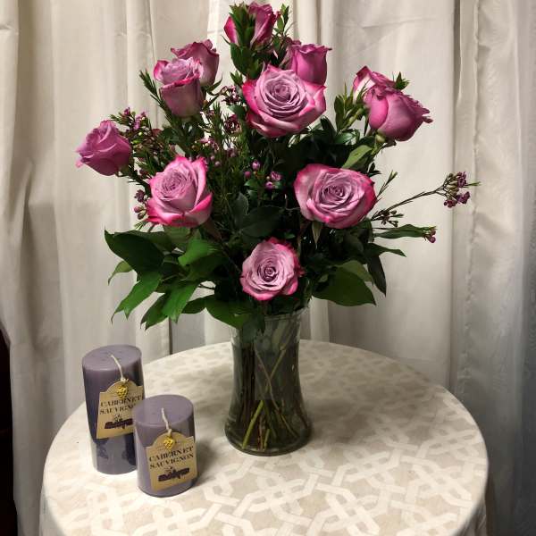 Pink roses arranged in a glass vase with two purple candles beside it