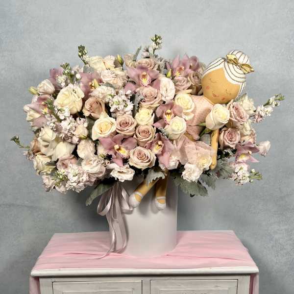 Large pastel pink and cream flower arrangement in a white hatbox with a plush ballerina doll nestled among the blooms