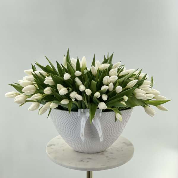 White tulips arranged in a textured white bowl vase