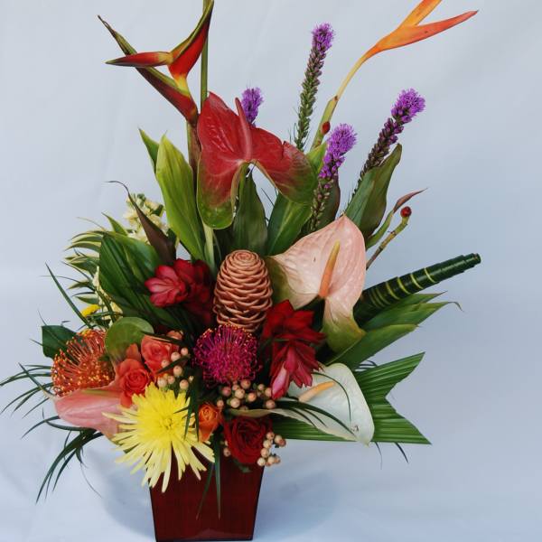 Tropical flower arrangement in a red vase with anthuriums and orchids
