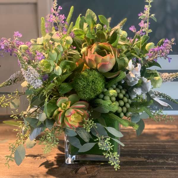 Mixed floral arrangement in a square glass vase with green succulents and purple accents