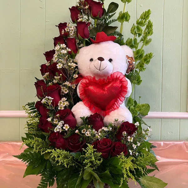Red roses arranged around a teddy bear holding a heart