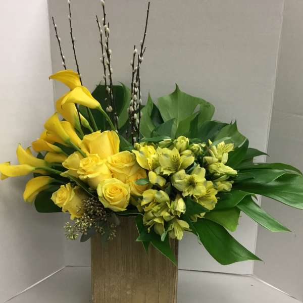 Yellow calla lilies and roses in a gold rectangular vase