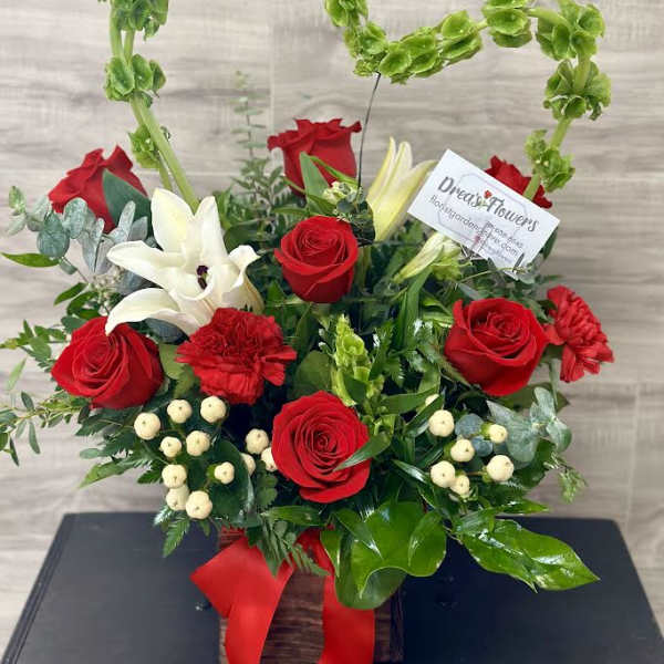 Red roses and white lilies in a wooden basket with a red ribbon