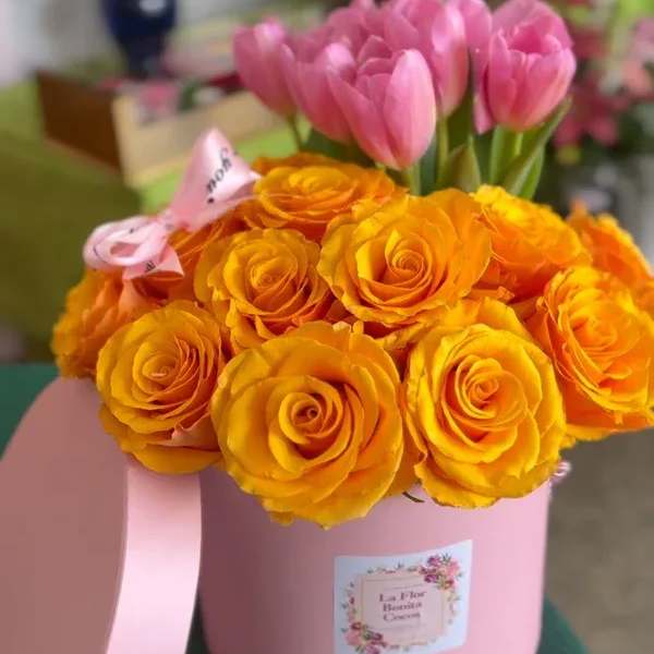 Pink tulips and orange roses in a pink hatbox with ribbon