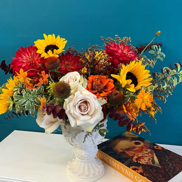 Colorful bouquet with sunflowers, roses, and orange blooms in a white vase