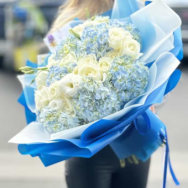 Bouquet of white roses and blue hydrangeas wrapped in blue paper