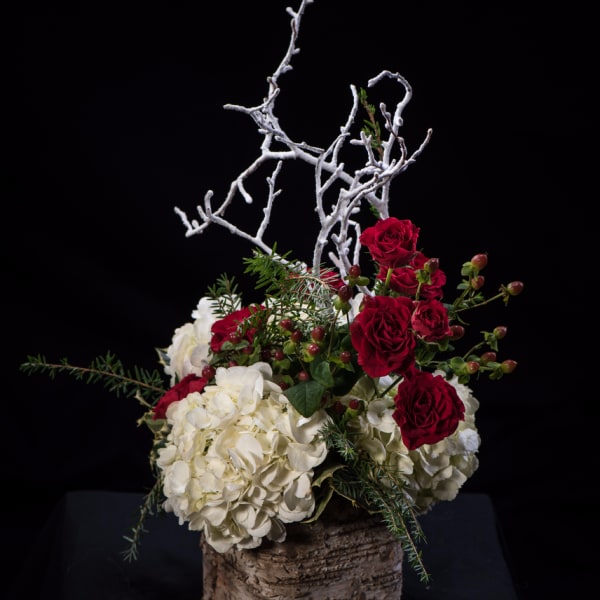 Red roses and white hydrangeas in a rustic bark container with white branches