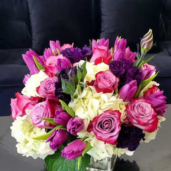 Low arrangement of pink and purple roses and tulips with white hydrangea in a clear glass cube vase