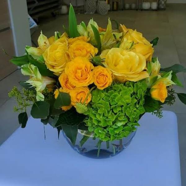 Low round arrangement of yellow roses and green hydrangea in a clear glass bowl vase