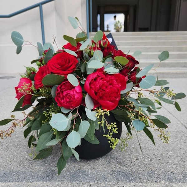 Low arrangement of red roses and peonies with eucalyptus in a round black vase