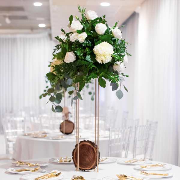 White floral centerpiece on a tall gold stand at a decorated table