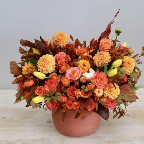 Low orange and yellow autumn flower arrangement with roses and dahlias in a terracotta pot.