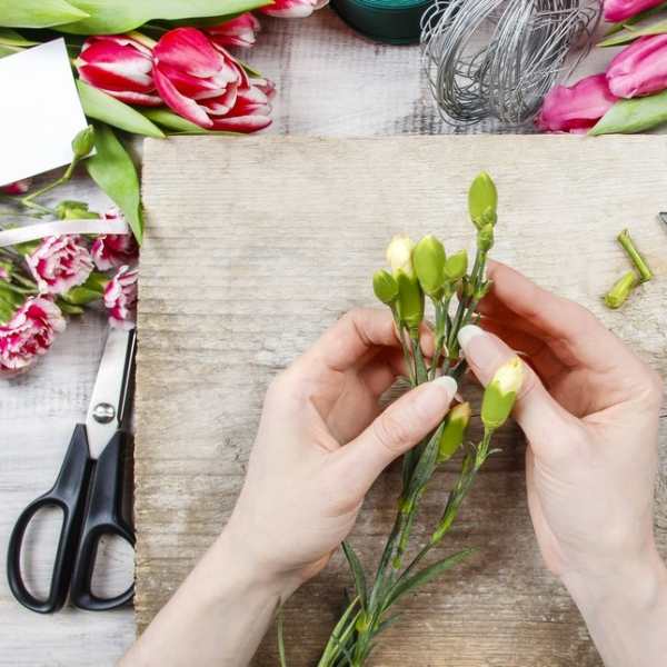 Hands arranging pink tulips and carnations with floral shears on a work surface