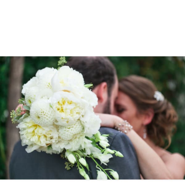 White bridal bouquet with trailing blooms held by a couple embracing