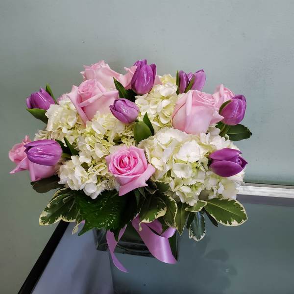 Pink roses and purple tulips arranged in a glass vase