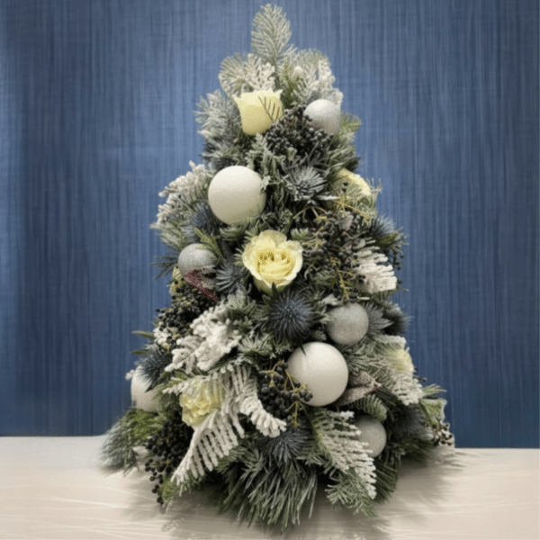 Snow-dusted Christmas tree arrangement with pale yellow roses and white ornaments