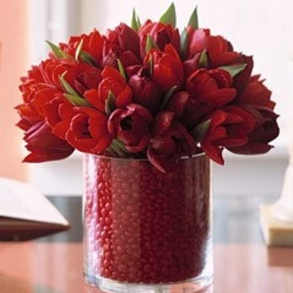 Red tulips arranged in a clear glass vase filled with red beads