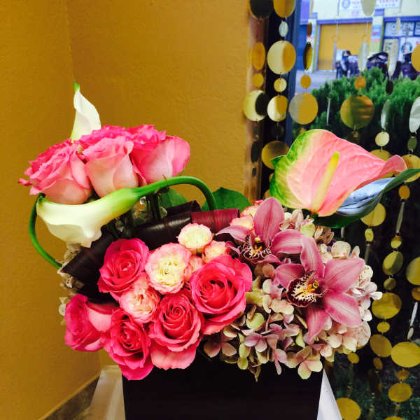 Pink roses and orchids arranged in a black box with white calla lilies