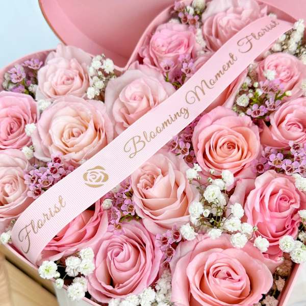 Pink roses arranged in a heart-shaped box with a ribbon