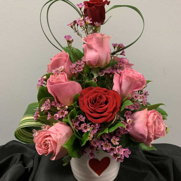 Pink and red roses in a white heart vase with a heart-shaped wire accent