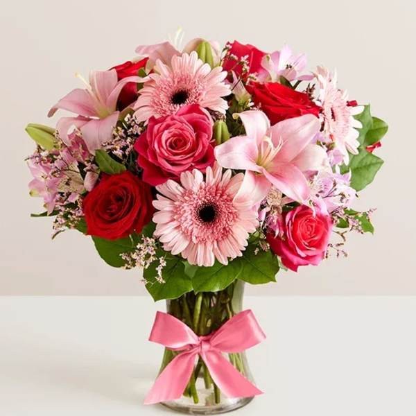 Pink and red mixed flower bouquet in a glass vase with a pink ribbon