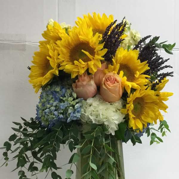 Sunflower and rose arrangement in a clear vase with trailing greenery