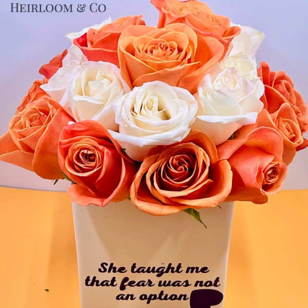 Orange and white roses arranged in a white vase with printed text