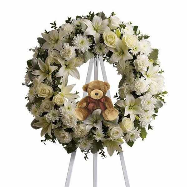 White floral wreath on an easel with a teddy bear in the center