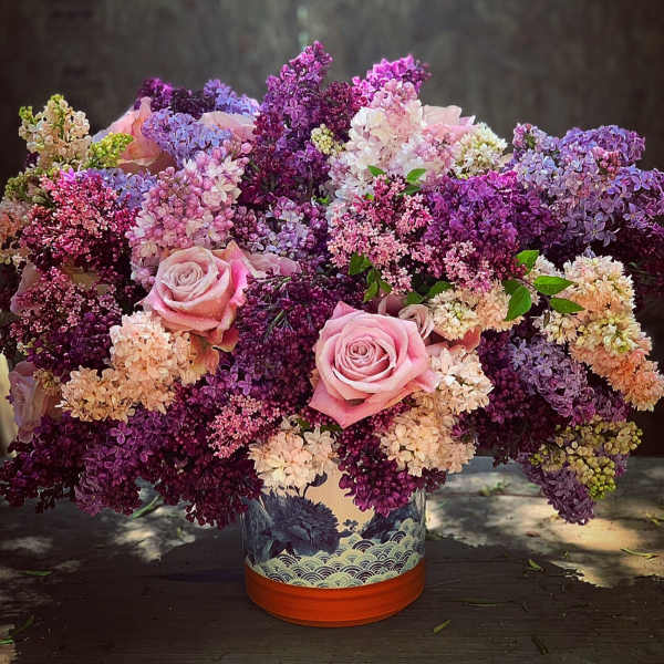 Pink roses in a decorative vase surrounded by purple and lavender blossoms