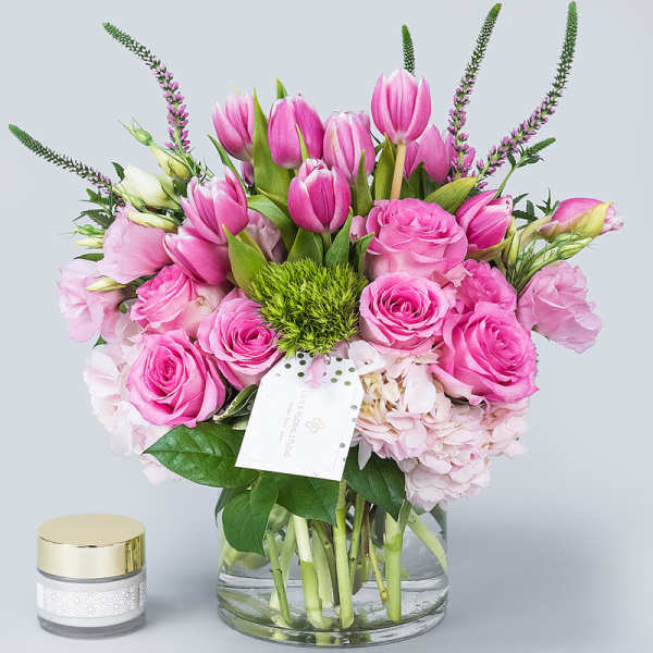 Pink tulips and roses arranged in a glass vase with a small candle beside it