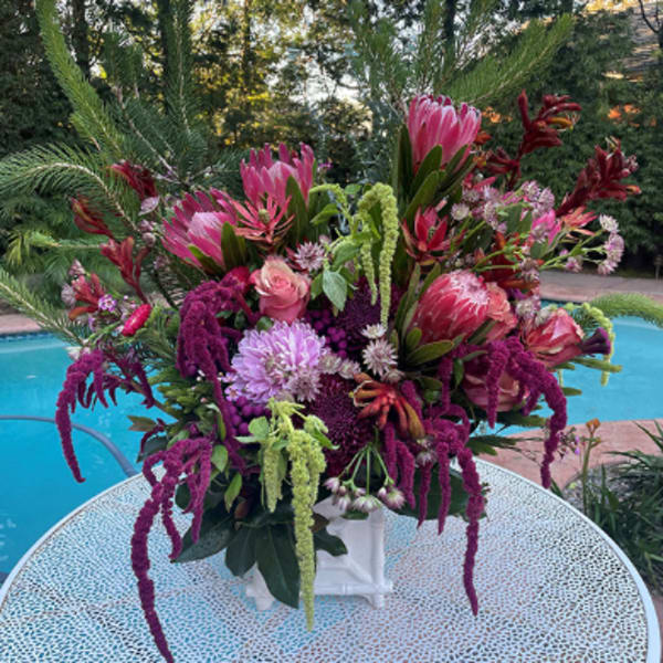 Large pink and purple floral arrangement in a white vase outdoors