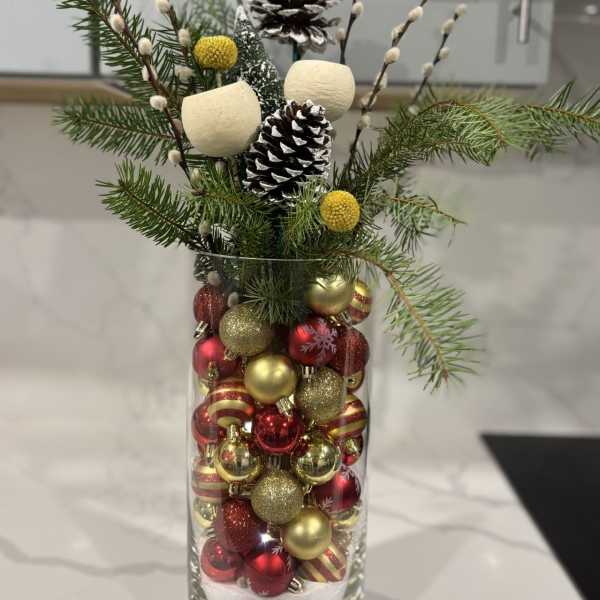 Holiday arrangement in a glass vase with pinecones and red-gold ornaments