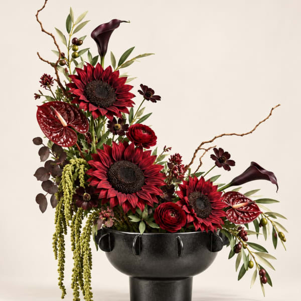 Red and burgundy floral arrangement in a black pedestal vase
