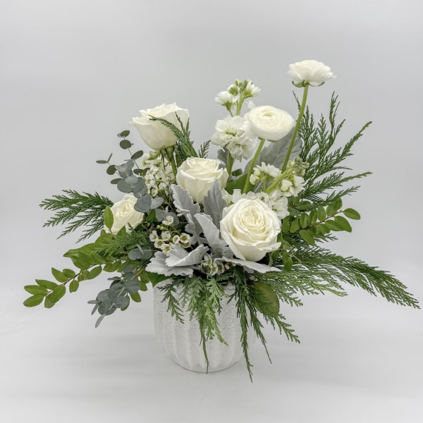 White roses and ranunculus in a white vase with mixed greenery