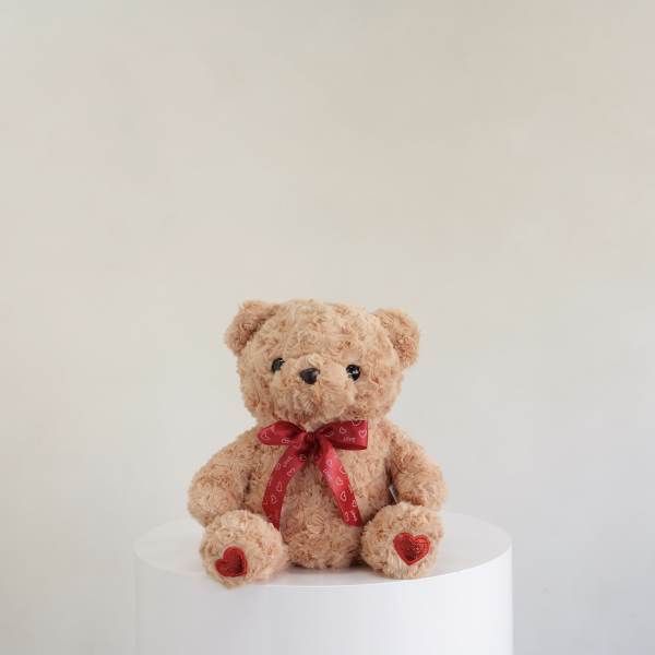 Plush teddy bear with a red heart ribbon sitting on a white pedestal