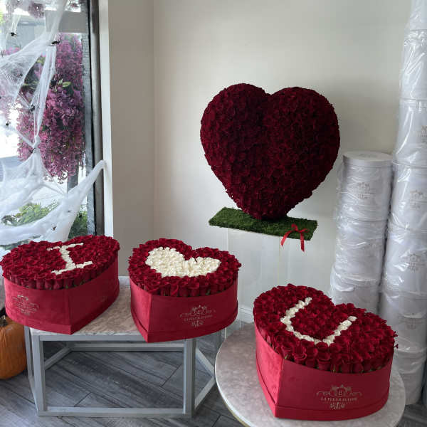Heart-shaped red rose arrangements in pink boxes and on a stand
