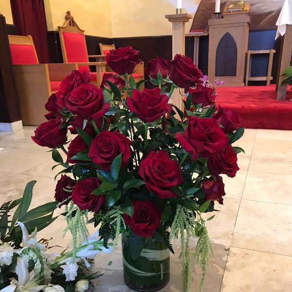 Red roses arranged in a glass vase with trailing greenery