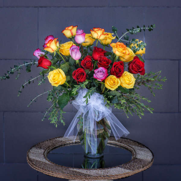 Bouquet of multicolored roses in a glass vase with a white bow