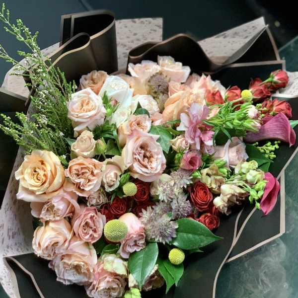 Bouquet of blush and peach roses with pink accents wrapped in black paper
