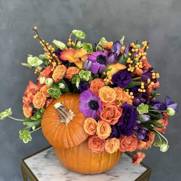 Orange pumpkin centerpiece with purple and orange flowers