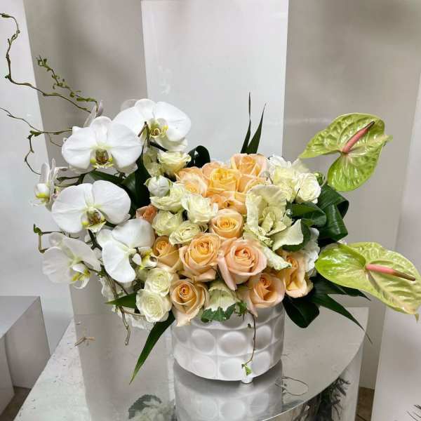 White orchids and peach roses in a white vase with green anthuriums